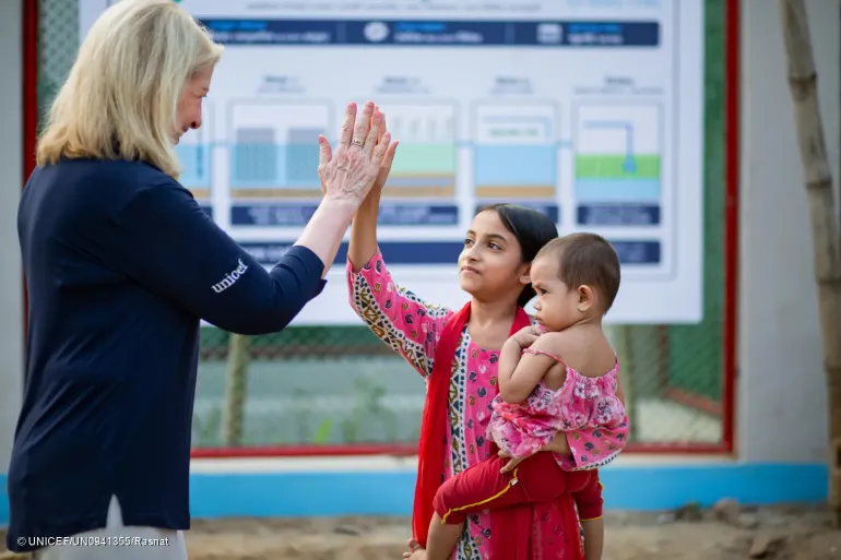 UNICEF's Executive Director shares a high-five with a young girl holding a small child during a field visit.