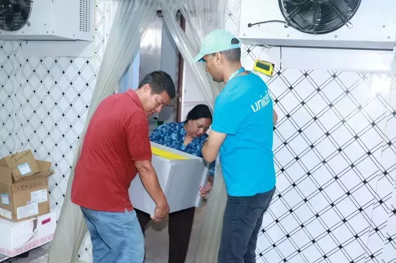 Three people carry a box with cholera vaccine.