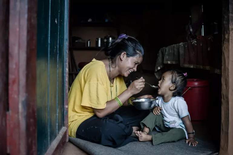 Swastika feeding her daughter home cooked meal, with rice, lentils and vegetables.
