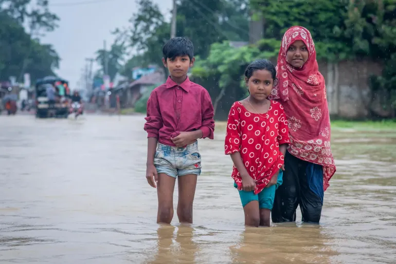 Three children stand knee deep in floodwater.
