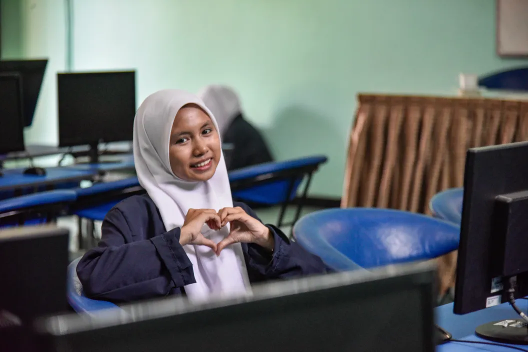 Reina Sulistyani Arifin, age 16, shares her motivation to join the digital literacy class initiated by UNICEF at her school. In the photo she smiles at the camera and gestures a heart with her hands