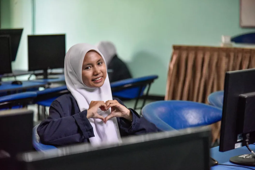 Reina Sulistyani Arifin, age 16, shares her motivation to join the digital literacy class initiated by UNICEF at her school. In the photo she smiles at the camera and gestures a heart with her hands