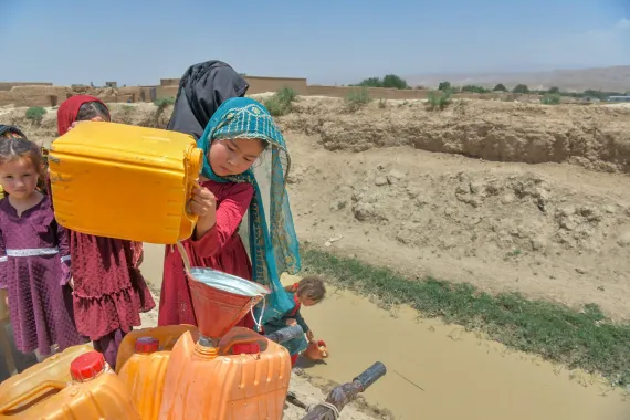 in the desert, a little girl pours water into a jerry can