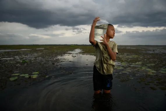 a boy carries a jug of fresh water on his shoulder through a flooded field