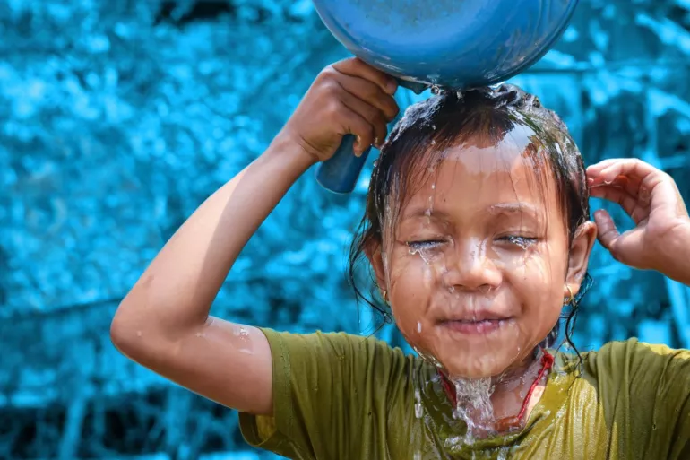 Un enfant se vide une bassine d'eau bleu sur la tête. 