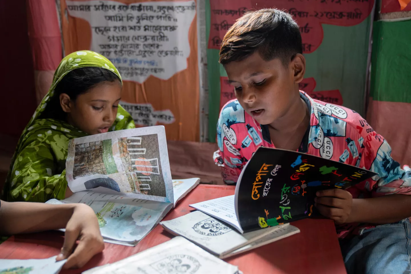 A boy and a girl read books in their classroom.
