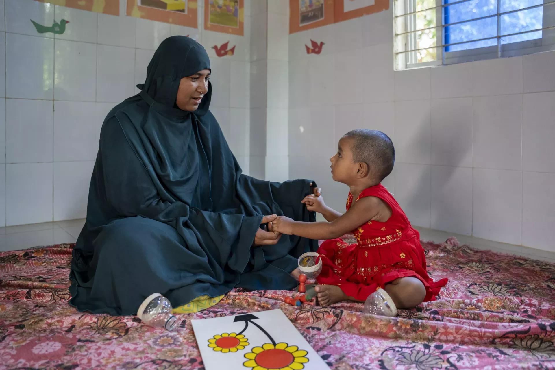 Fahima Begum sits beside her 18-month-old daughter, Roza, while pointing at a flower in a puzzle card.