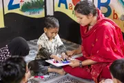 A caregiver supports Muhammad during a learning activity at the UNICEF-supported Surabari Day-care Center.