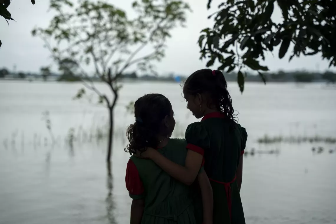 From the alternative learning space, Tania and Tawhida gaze at floodwaters stretching to the horizon. Attending school offers them a brief escape from the hardships that natural disasters leave behind. 