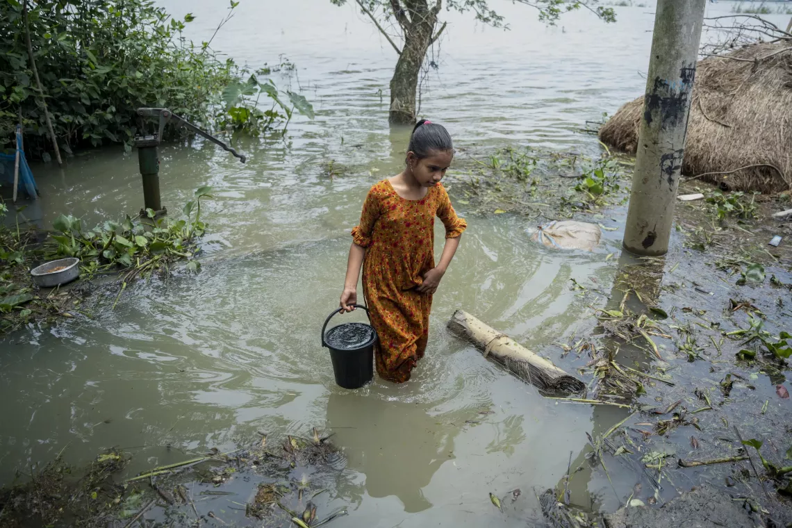 Tawhida wades through floodwater to bring drinking water home. 