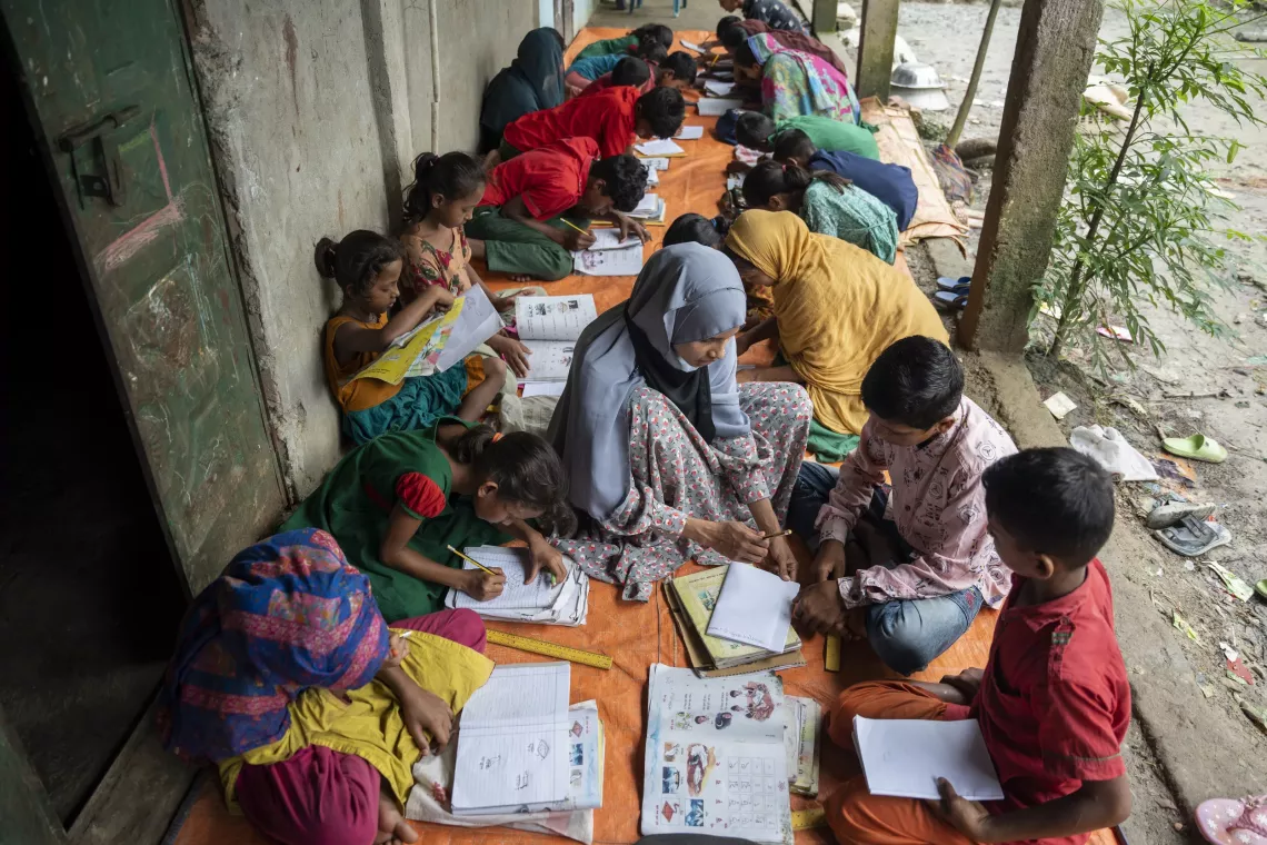 Children gather around Husna, attentively listening to her guidance. The alternative learning space was set up to ensure they can keep learning. 