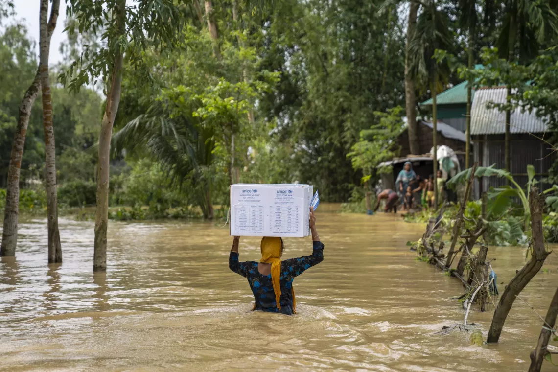 A woman wades through floodwater on her way back home after receiving hygiene kits from UNICEF in Nalitabari, Sherpur. 