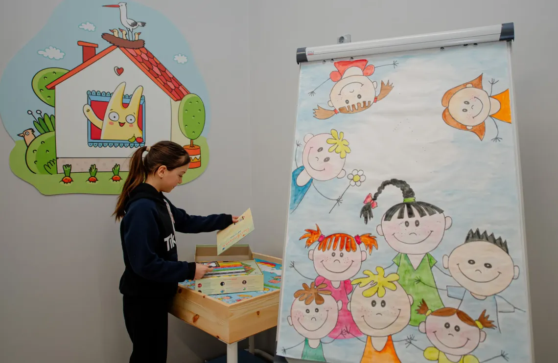 Девочка открывает настольную игру в Комнате, дружественной детям