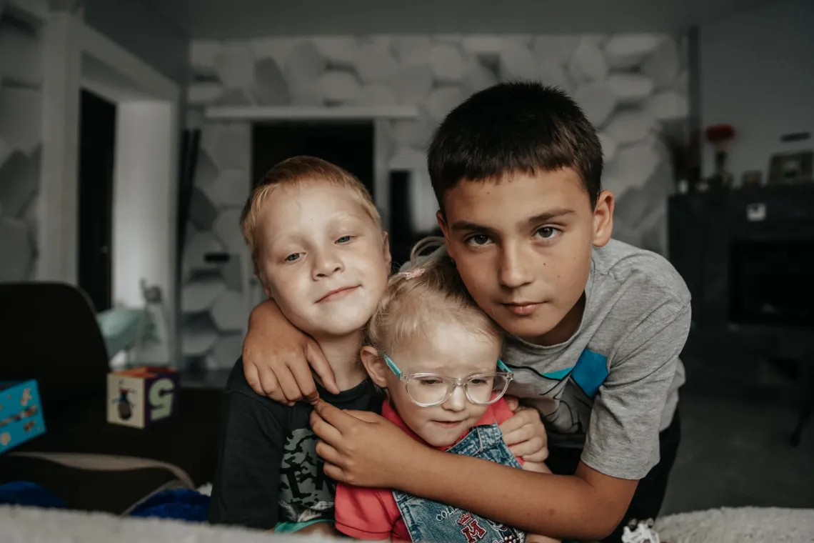 Двое мальчиков и девочка позируют фотографу у себя дома
