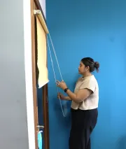 woman stands holding string for window blinds