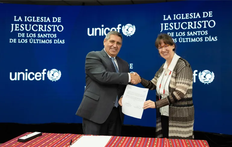 Dos personas d&aacute;ndose la mano mientras sostienen un documento