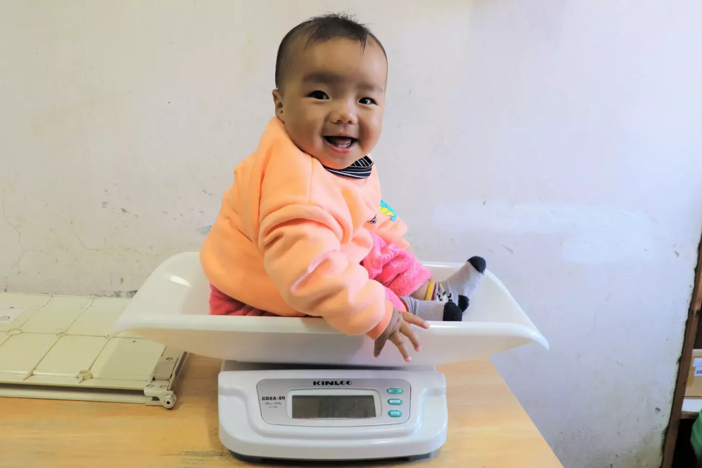 A child smiles as she gets weighed at a health center