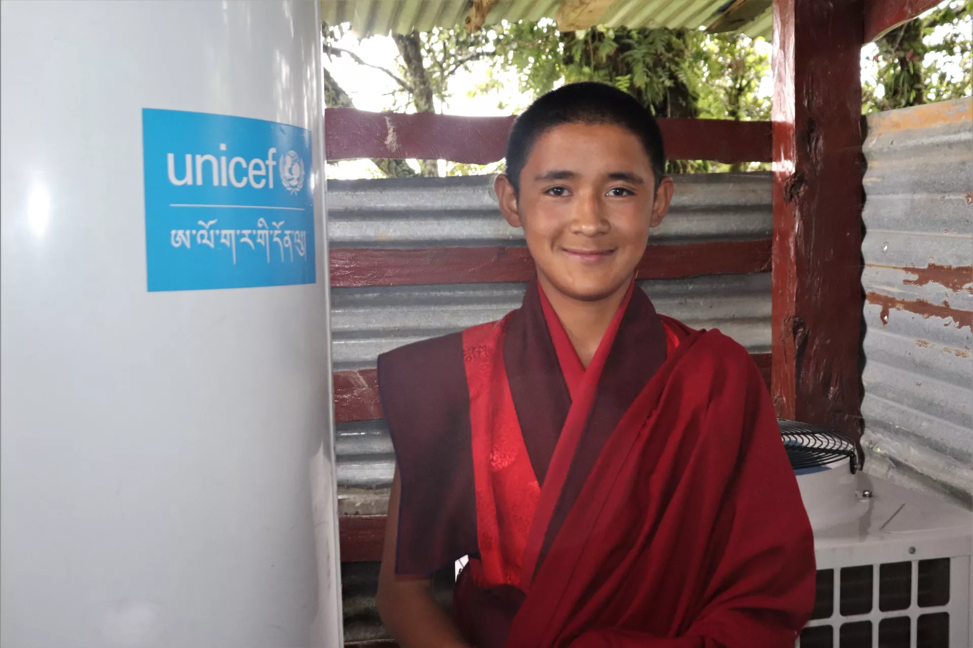 A young monk smiles next to a heat pump