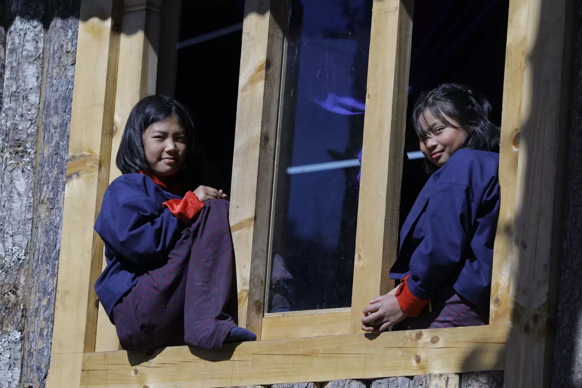 Two girl students sit on the ledge of a window