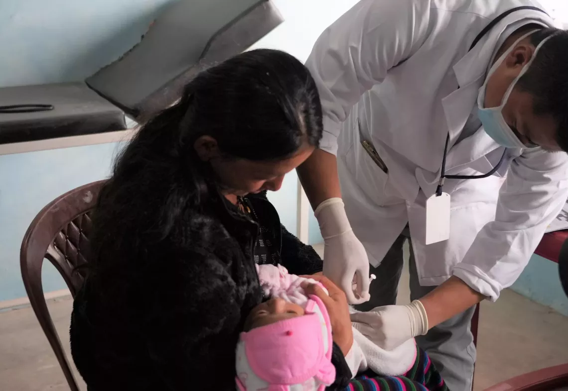 A man injects a child as the mother holds the baby on her lap.