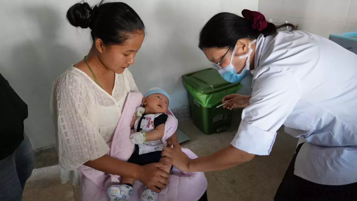 Devi Maya holds her son as the health assistant prepares to inject a vaccine at Norbugang Primary Health Center in Samtse district. 