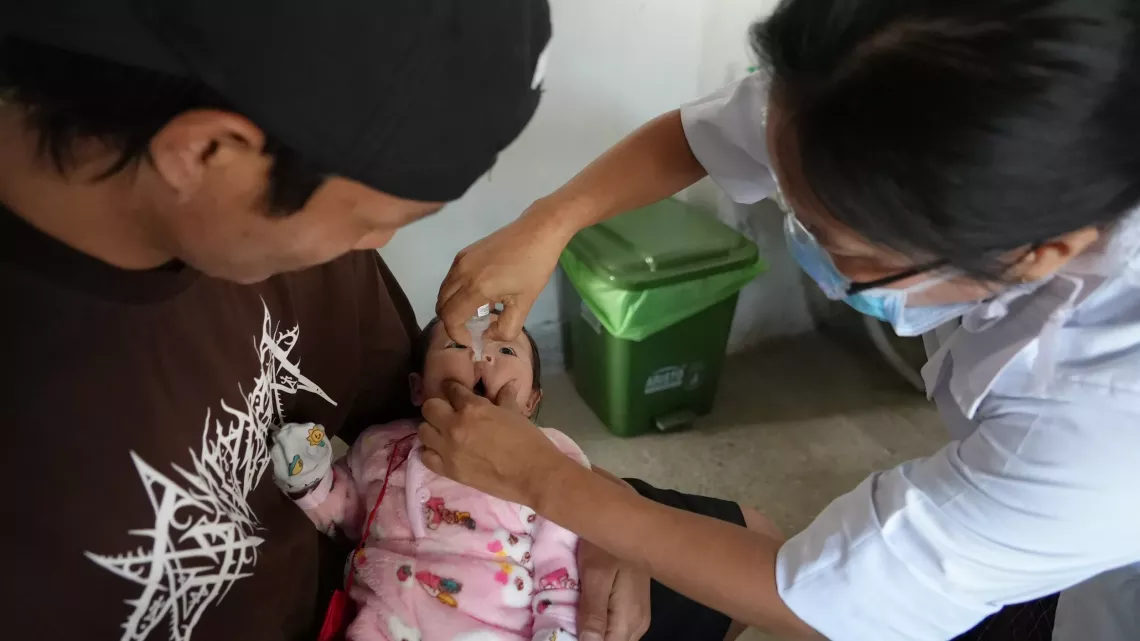 Chencho Wangchuk holds his son as he receives the polio drop at Norbugang Primary Health Center in Samtse district.
