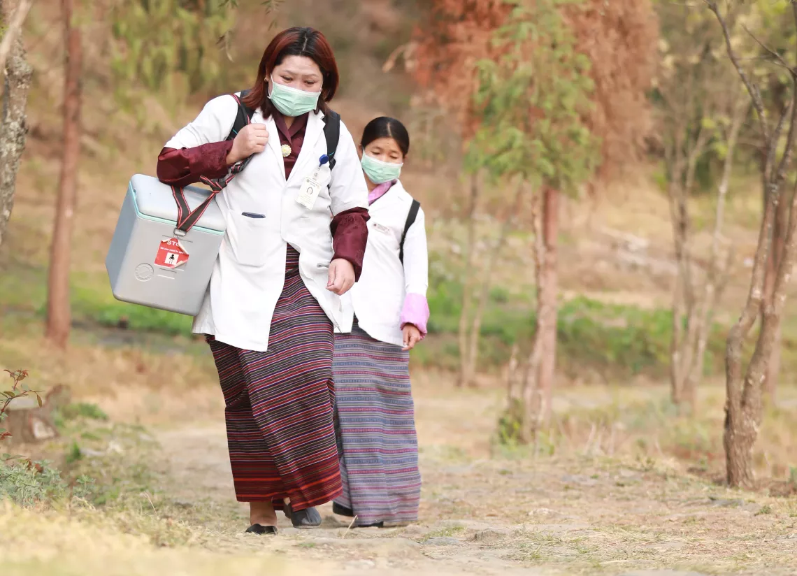 Two nurses walk with the vaccine carriers in Dagana