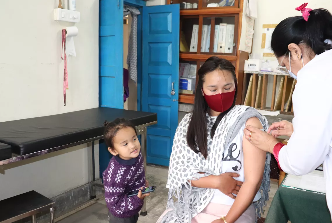 A child looks on as his mother gets vaccinated.