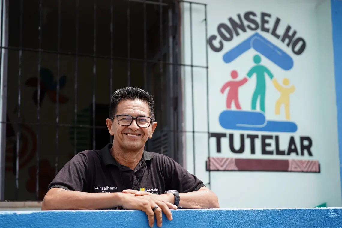 homem apoia bra&ccedil;os em muro em frente a uma placa do conselho tutelar