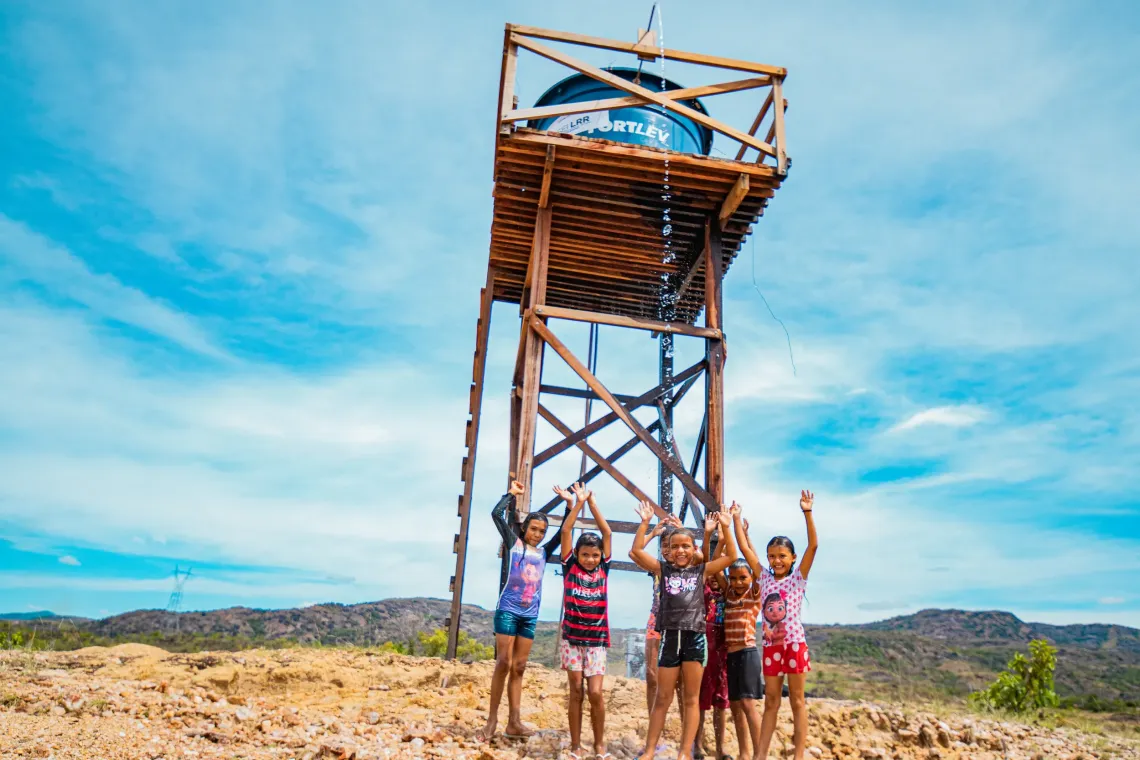 crian&ccedil;as brincam e celebram com bra&ccedil;os pra cima em frente a caixa d'&aacute;gua com logo do UNICEF