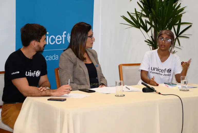 tr&ecirc;s pessoas sentadas nem uma mesa vestindo camisetas do UNICEF