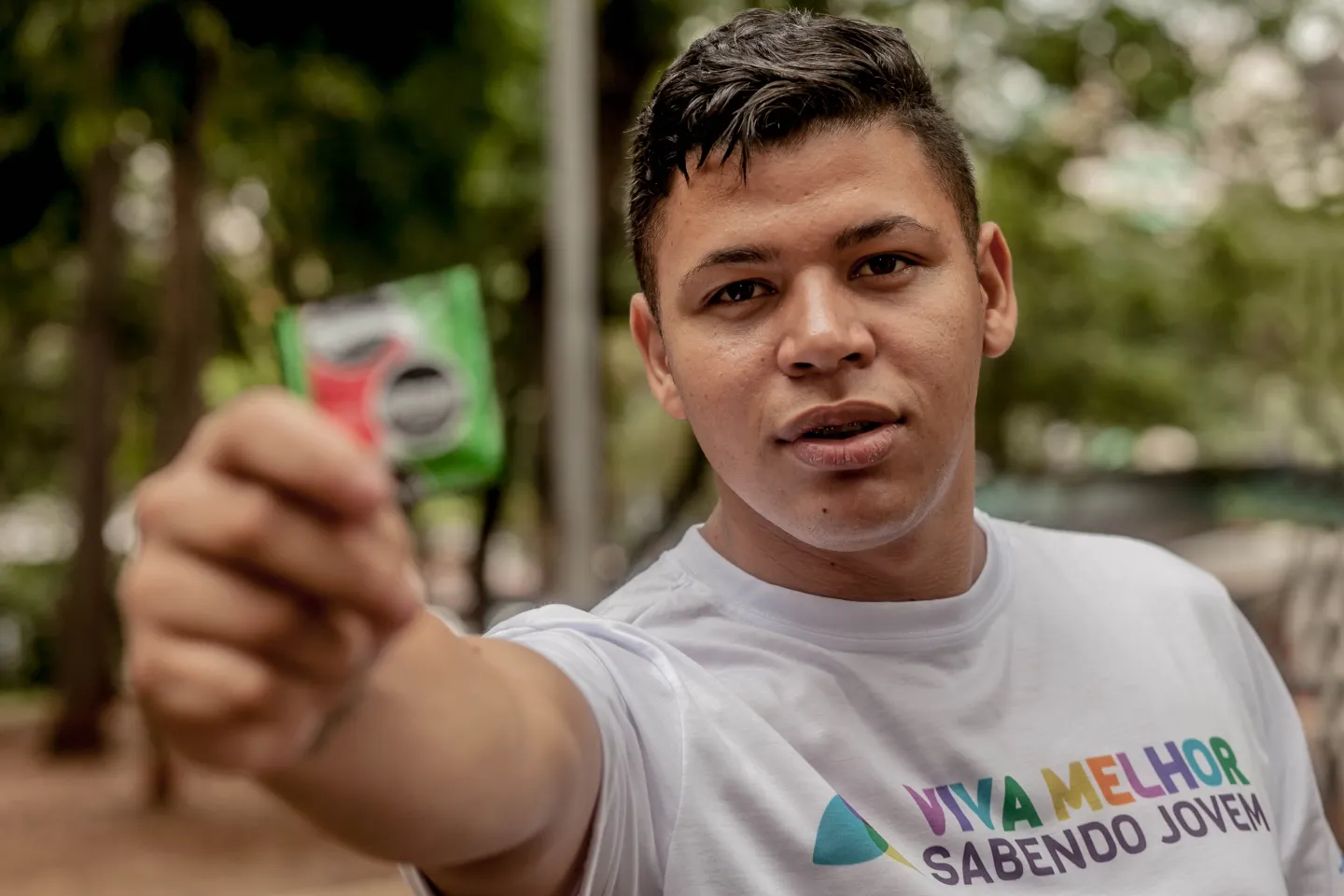 Renato com a camiseta do projeto Viva Melhor Sabendo Jovem segura um pacote de preservativo na m&atilde;o direita