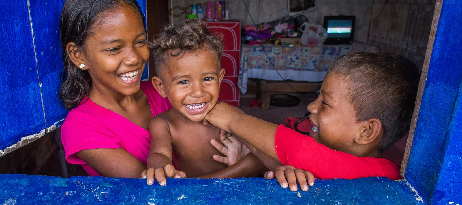 Tr&ecirc;s irm&atilde;os - uma menina e dois meninos - na janela de sua casa