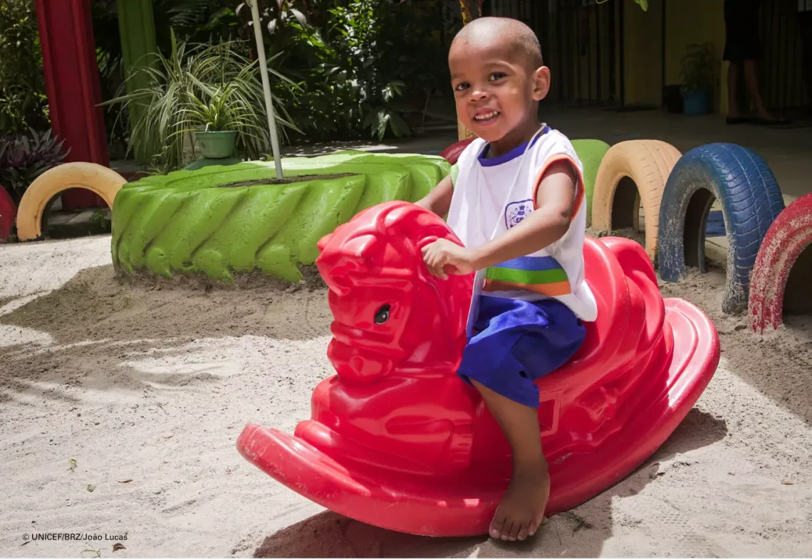 Crian&ccedil;a em cima de cavalo de brinquedo de pl&aacute;stico vermelho em parquinho da escola