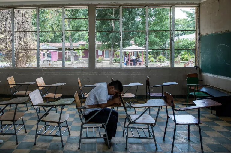 Adolescente sentado sozinho na sala de aula, apoiando a cabe&ccedil;a na carteira escolar. Foto de Honduras