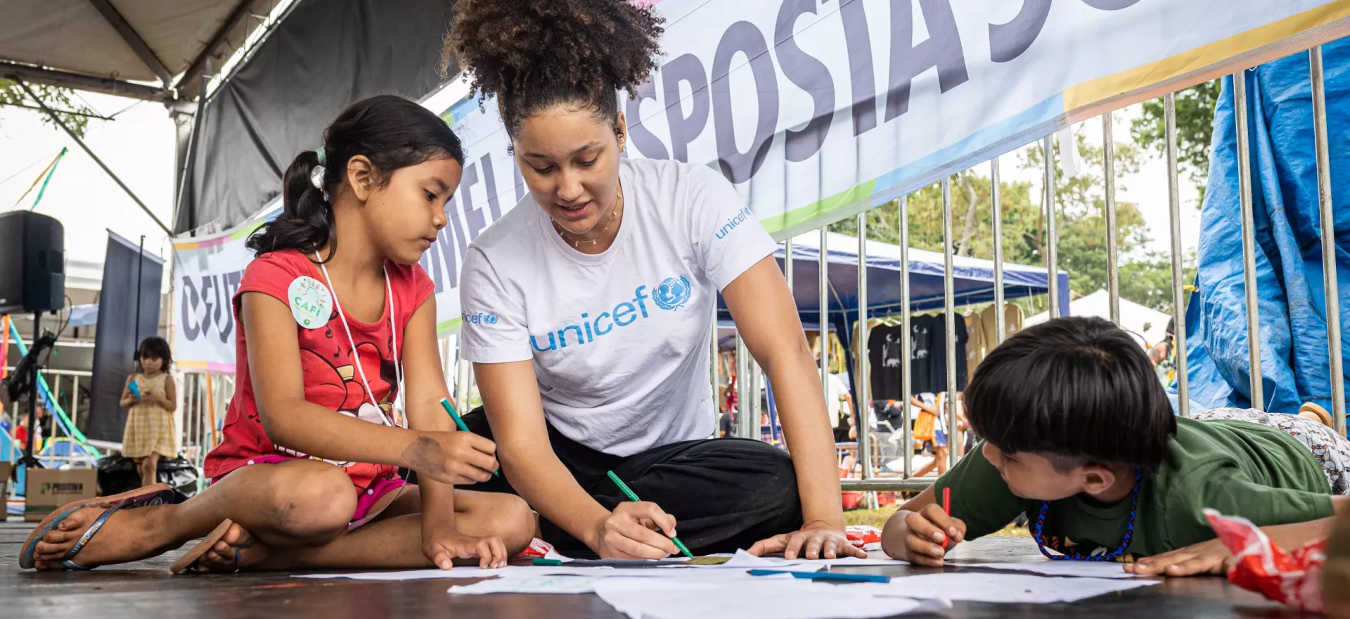 funcion&aacute;ria do UNICEF desenha ao lado de duas crian&ccedil;as ind&iacute;genas