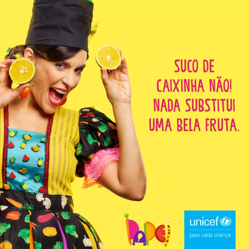 Card com fundo amarelo, foto de uma mulher segurando uma fruta, escrito em vermelho Suco de caixinha n&atilde;o! Nada substitui uma bela fruta. No canto inferior direito aparecem os logos da campanha e do UNICEF.