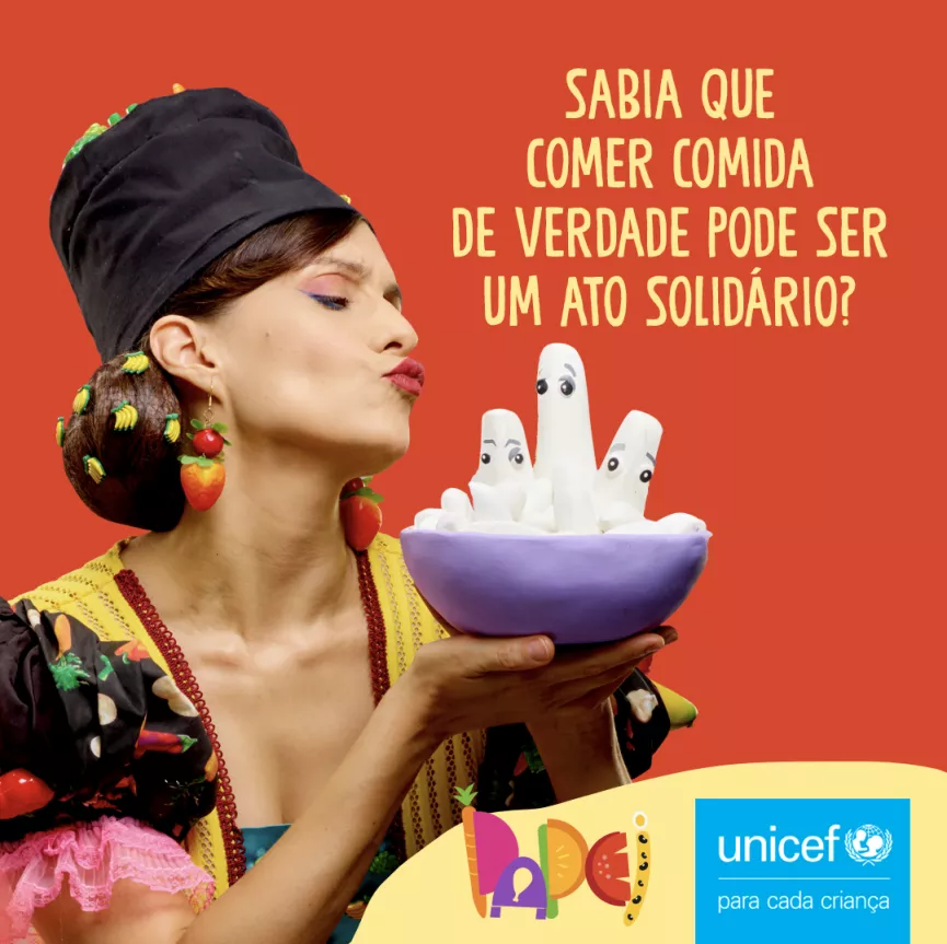Card com fundo vermelho mostra a personagem Miranda segurando uma tigela. Em amarelo est&aacute; escrito: Sabia que comer comida de verdade pode ser um ato solid&aacute;rio?. No canto inferior direito aparecem os logos da iniciativa e do UNICEF.