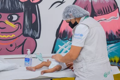 Profissional de sa&uacute;de vestindo uma camiseta com a logomarca do UNICEF examina um beb&ecirc; em uma maca