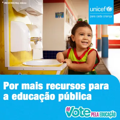 Card da campanha #VotePelaEduca&ccedil;&atilde;o - No canto superior direito aparece o logo do UNICEF. No rodap&eacute; da imagem aparece o logo da campanha e est&aacute; escrito Por mais recursos para a educa&ccedil;&atilde;o p&uacute;blica. Foto mostra uma menina em idade pr&eacute;-escolar parada do lado de uma pia. Ela est&aacute; olhando para algu&eacute;m na frente dela (que n&atilde;o aparece na foto) e est&aacute; sorrindo.