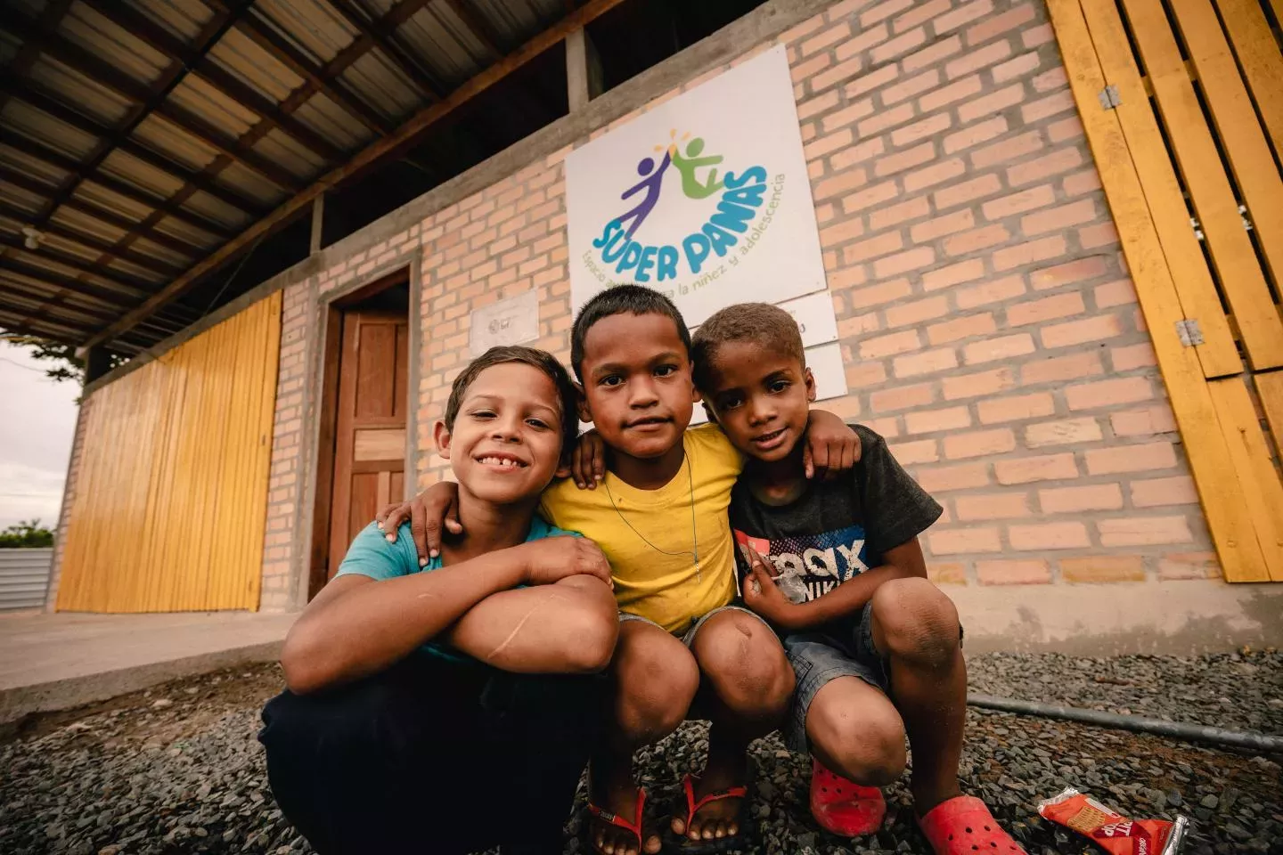 Tr&ecirc;s meninos se abra&ccedil;am em frente a espa&ccedil;o com placa do SUper Panas