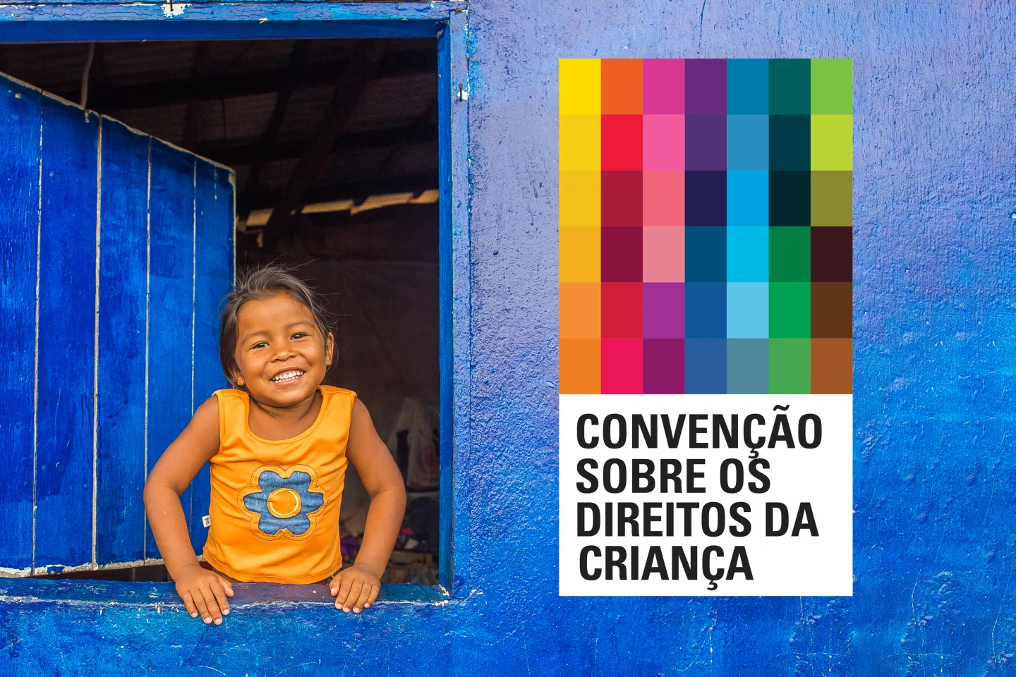uma menina pequena na janela sorri para a c&acirc;mera, ao lado dela um p&ocirc;ster cheio de ret&acirc;ngulos coloridos e o nome Conven&ccedil;&atilde;o sobre os Direitos da Crian&ccedil;a