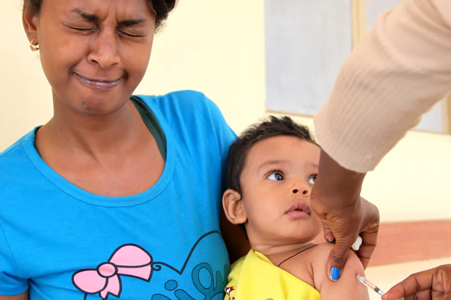 Uma mulher faz careta quando um profissional de sa&uacute;de vacina seu filho contra o sarampo na Eritreia 