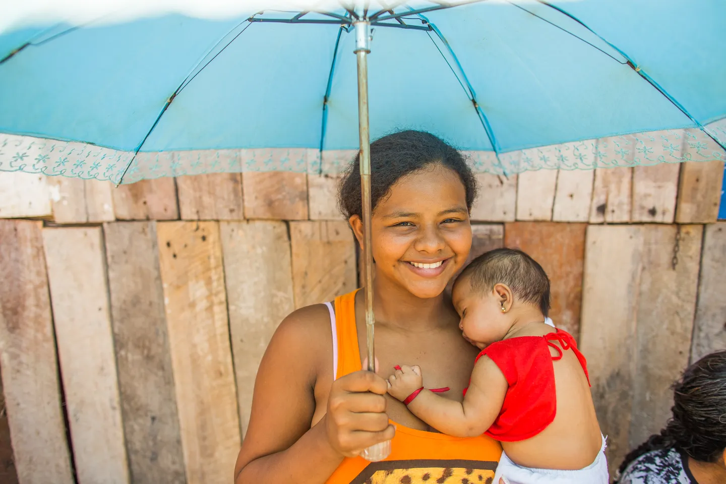 Mulher carrega sua filha beb&ecirc; no colo. Elas est&atilde;o embaixo de um guarda-chuva