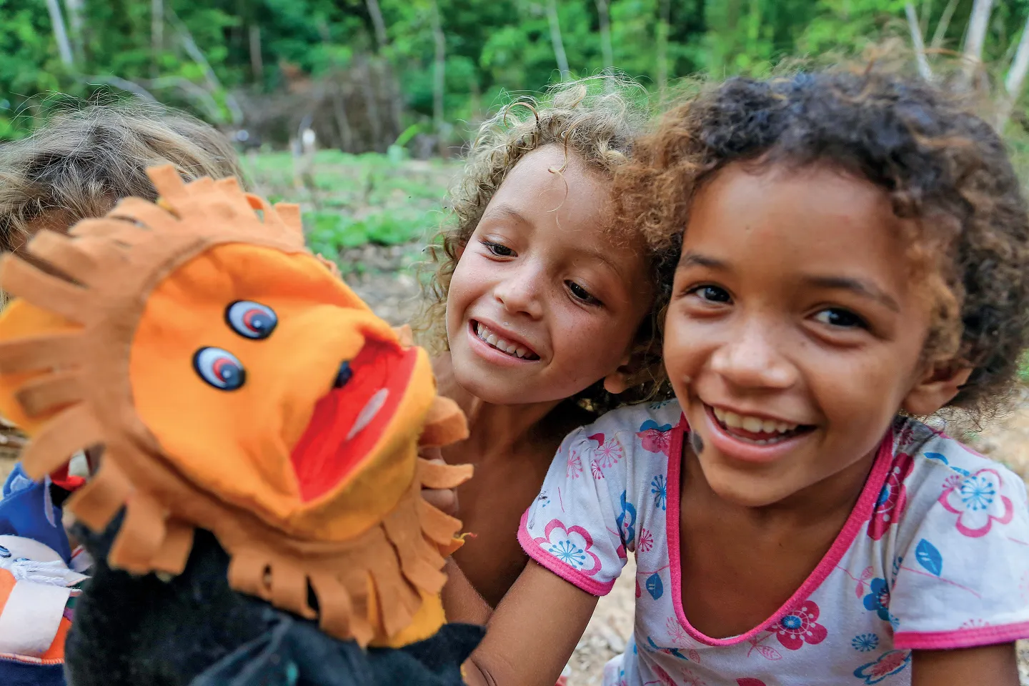 duas crian&ccedil;a brincam com marionetes ao ar livre. elas sorriem.