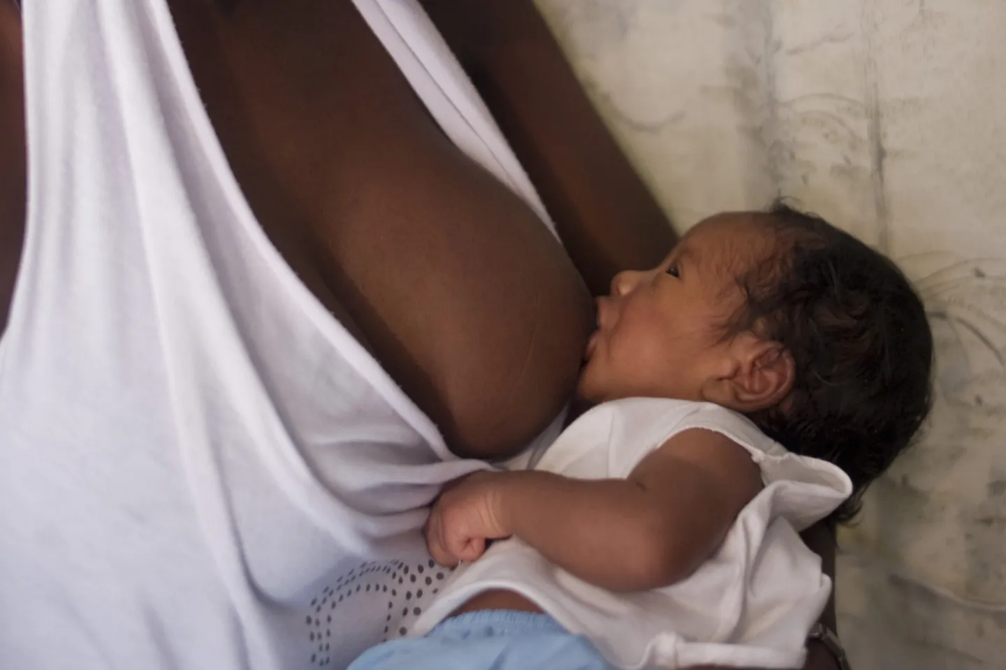 foto mostra um beb&ecirc; sendo amamentado. n&atilde;o aparece o rosto da m&atilde;e. o beb&ecirc; est&aacute; olhando para o rosto dela.