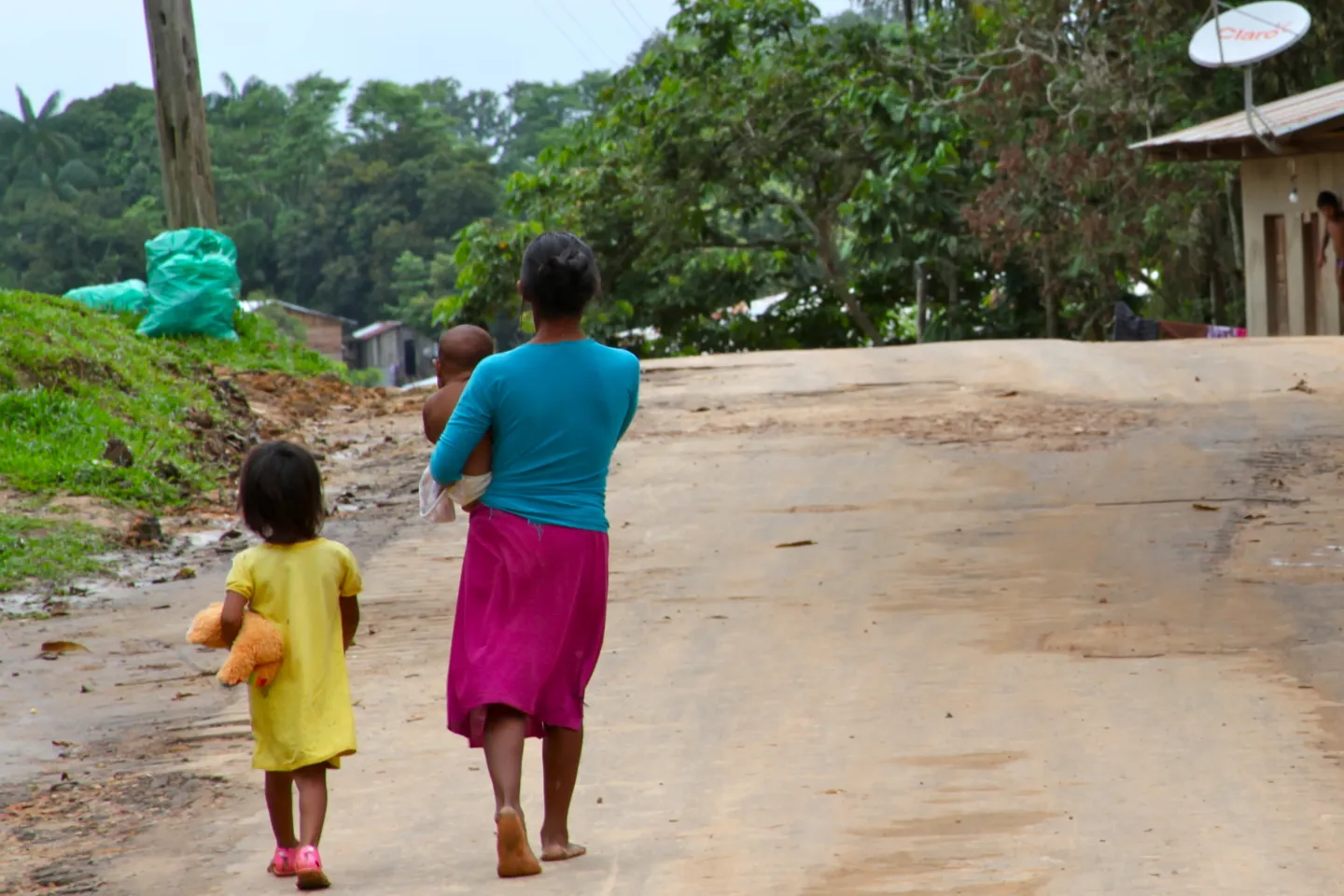 Mulher ind&iacute;gena caminha em estrada de terra com seu beb&ecirc; no colo e sua filha pequena ao lado