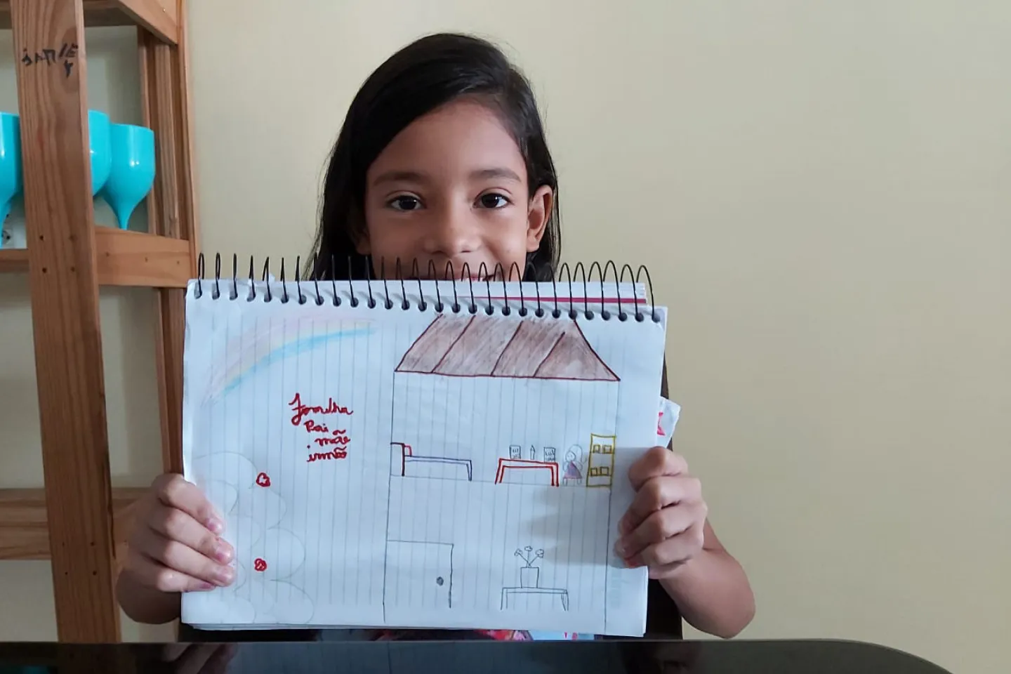 Menina sorridente mostra um desenho de uma casa