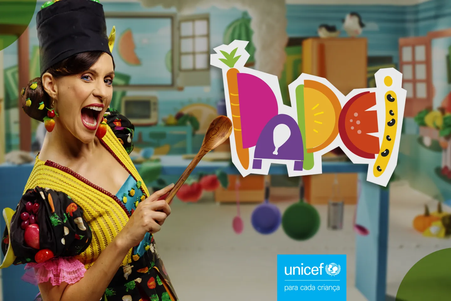 Imagem mostra uma mulher segurando uma colher de pau. No fundo h&aacute; uma cozinha desfocada. Do lado direito aparece o logo da campanha, Papei escrito com frutas, e o logo do UNICEF.
