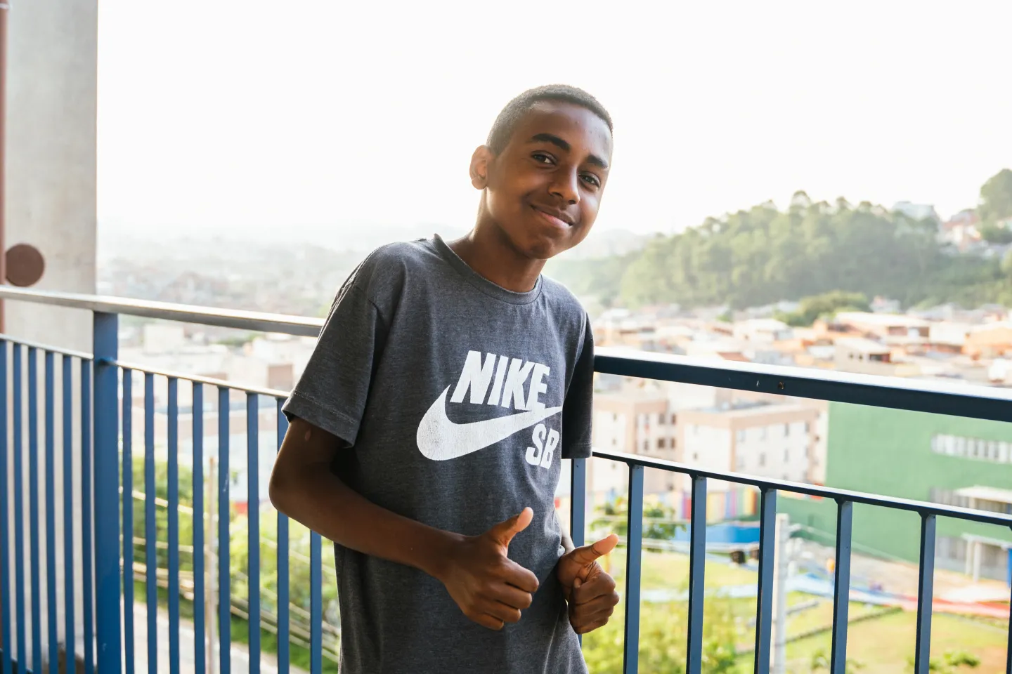 Foto mostra um adolescente apoiado em uma grade.